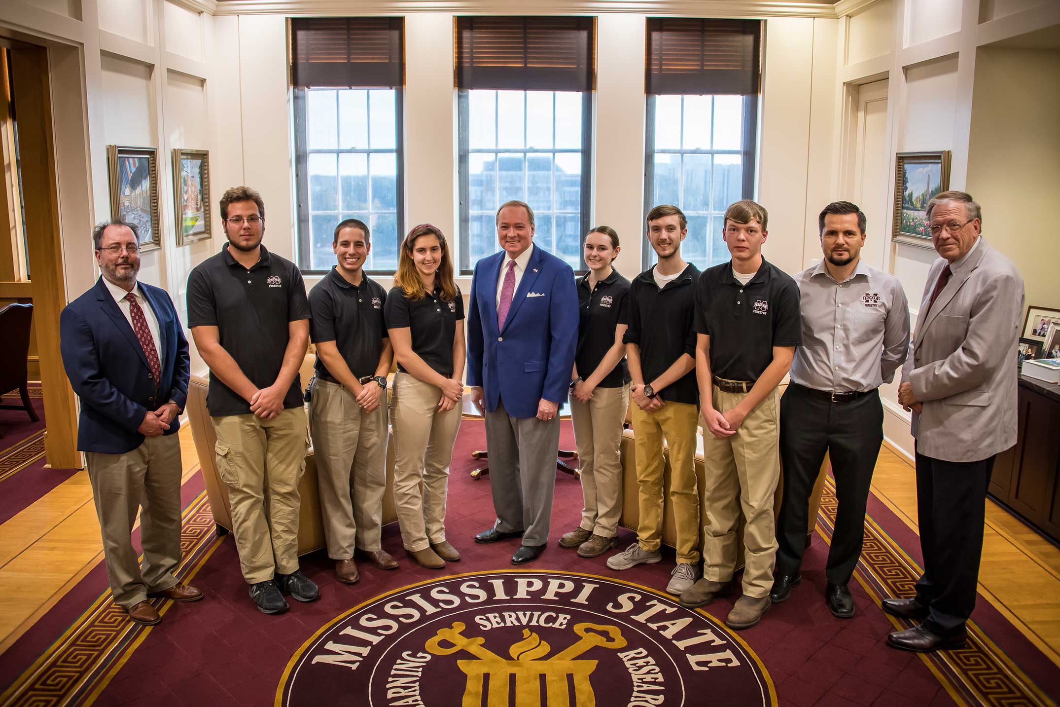 Six forestry students and four men stand on carpet with the MSU displayed.