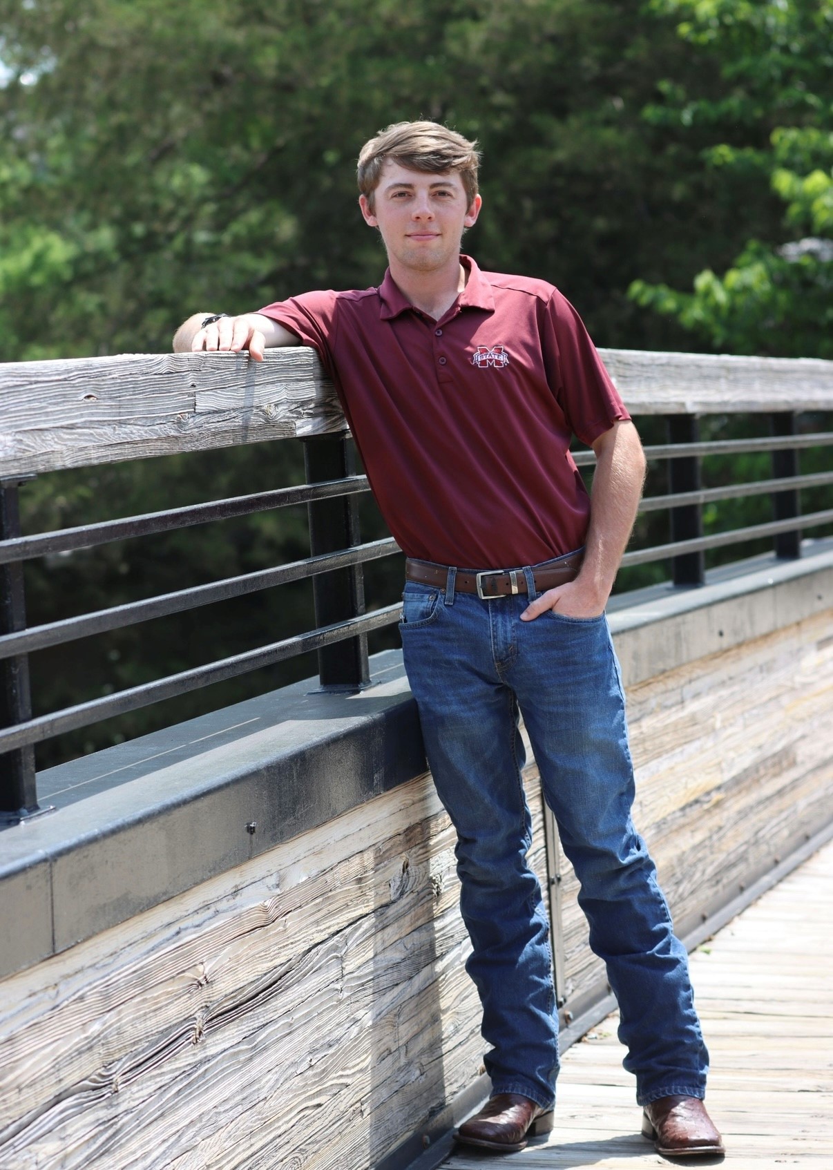 MSU graduate with maroon shirt on bridge leaning on rail