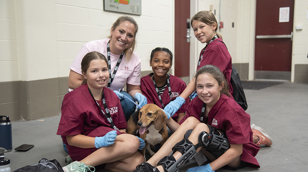 Four students and instructor sit around a dog at Vet Camp.